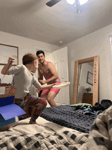 a man in a bathing suit holds a frisbee while another man squats on the bed