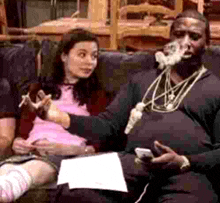 a man is smoking a cigarette while sitting on a couch while a woman looks on .