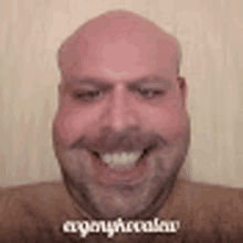 a bald man with a beard is smiling and making a funny face .