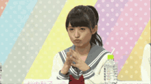 a girl sitting at a table with a polka dot background and a bottle of water in front of her