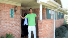 a man in a green shirt is standing in front of a brick house with a blue sign that says ' mr. '