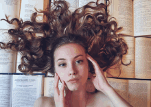 a woman laying on top of a pile of books with her hair covering her face and head