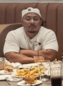 a man wearing a white hat sits at a table with plates of food