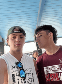 a man wearing a saints hat is standing next to another man wearing a maroon all star t-shirt