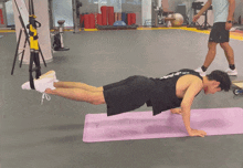 a man in a black tank top is doing push ups on a purple mat in a gym