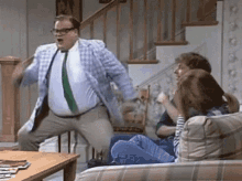 a man in a suit and tie is dancing in a living room while people sit on a couch .