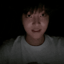 a close up of a person 's face in the dark wearing a white shirt