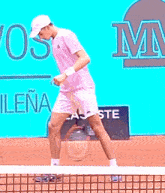 a man in a pink shirt and white hat is standing on a tennis court in front of a sign that says lacoste .