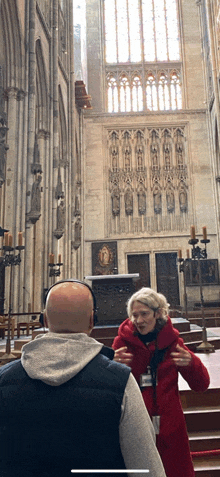 a woman in a red coat is talking to a bald man