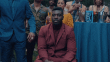 a man in a red suit sits in front of a table with a sign that says ' a ' on it