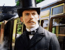 a man with a top hat and mustache is standing in front of a train .