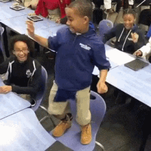 a young boy is standing on a chair in a classroom while a group of children sit at tables .