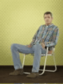 a man in a plaid shirt is sitting in a chair against a yellow wall .