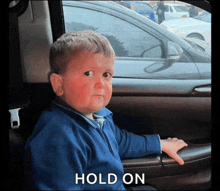 a young boy sitting in a car with the word hold on written on the bottom