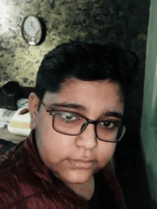 a young boy wearing glasses and a red jacket is taking a selfie in front of a clock .