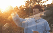 a man in a blue shirt is blowing soap bubbles in a field with the sun shining through the trees behind him