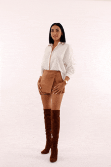 a woman wearing a white shirt and brown shorts stands in front of a white background