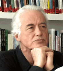 a man with white hair is sitting in front of a shelf of books including one titled recording in a foreign language