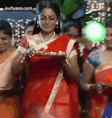 a woman in a red sari is holding a tray of food in front of a group of people .