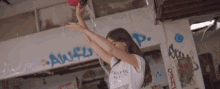 a girl in a white shirt is pouring water from a red bottle with the word aweful written on the wall behind her