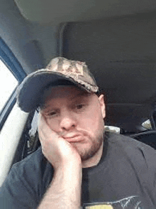 a man wearing a hat is sitting in the driver 's seat of a car with his hand on his chin .