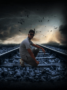 a man kneeling on train tracks with birds flying in the sky