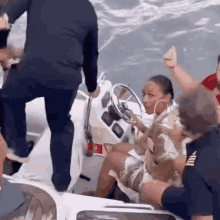 a woman is sitting at the steering wheel of a boat while a group of people are standing around her .