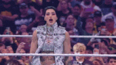 a woman in a white vest is standing in a wrestling ring .