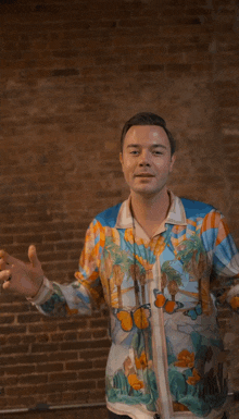 a man in a colorful shirt is standing in front of a brick wall with his arms outstretched