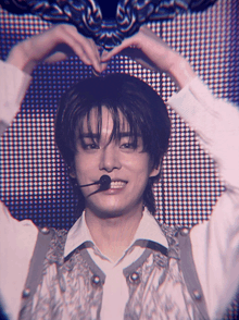a young man making a heart shape with his hands while wearing a microphone
