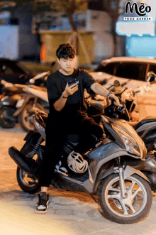 a man sitting on a motorcycle looking at his phone with a meo food garden logo in the background