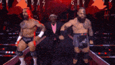 a man in a suit stands between two wrestlers wearing black shorts that say ' aoa ' on them