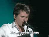 a man singing into a microphone with the words we will be victorious above him