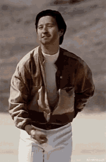 a man wearing a brown jacket and white pants is standing in the desert .