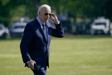 a man in a suit and tie is walking through a grassy field while talking on a cell phone .