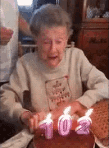 an elderly woman is blowing out candles on a birthday cake with the number 10 and 2 on it .