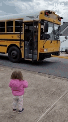 a little girl in a pink jacket stands in front of a school bus with the number 1753 on it