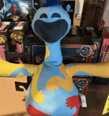 a blue and yellow stuffed animal with its arms outstretched is standing in front of boxes