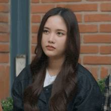 a young woman with long hair is sitting in front of a brick wall .