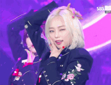 a woman with blonde hair and red nails is dancing in front of a purple background with sbs written on it