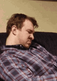 a man in a plaid shirt sleeps on a couch