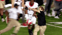 a man in a black shirt and khaki pants is running on a football field in front of a crowd