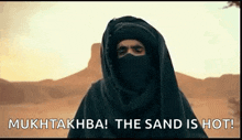 a man in a black turban is standing in the desert and says `` the sand is hot ! ''