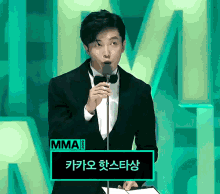 a man in a tuxedo stands in front of a microphone and a sign that says mma 2020