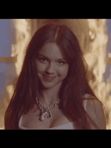 a close up of a woman wearing a necklace and a white top in front of a fire .