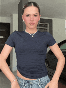 a woman wearing a blue t-shirt and jeans stands in front of a black car