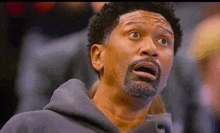 a man with a beard is making a surprised face while watching a basketball game .