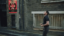 a man is running down a street in front of a brick building with a poster on the side .