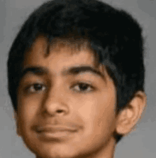 a close up of a young boy 's face with a gray background and a smile on his face .