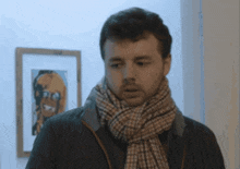 a man with a scarf around his neck is standing in front of a framed picture